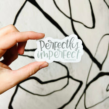 Load image into Gallery viewer, Text "perfectly imperfect" in two different colors. "Perfectly" is gray, and "imperfect" is green. The background color is white. The sticker is held by a white woman in front of a white backdrop with spiraling black lines.