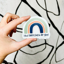 Load image into Gallery viewer, Dark blue text "Life is tough, but so are you!" under a four stripe rainbow. The inner stripe is thin and light pink, the next stripe is thick and dark blue, the third stripe is slightly less thick and salmon colored, and the last stripe is thicker and green. The sticker is held in front of a white wall with spiraling black lines by a white woman.