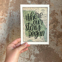 Load image into Gallery viewer, A vintage style map design of the state of Georgia with black lettered text "where our story began" over the print. The map is held in front of a brown rustic wall by a white woman.