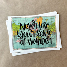 Load image into Gallery viewer, A stack of blue, green, yellow, and pink flat maps of the world with text "never lose your sense of wonder" in black lettering over the map print. The maps are lying on a large piece of brown paper.