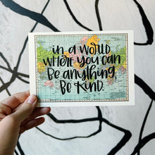 Load image into Gallery viewer, A blue, green, yellow, and pink flat map of the world with text "in a world where you can be anything, be kind" in black lettering over the map print. The map is held by a white woman, in front of a white background with spiraling black lines.