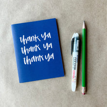 Load image into Gallery viewer, A dark blue card with white text "thank ya" printed three times on three separate lines. The card is lying on a piece of brown paper beside a pencil and a pen.