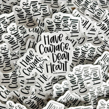 Load image into Gallery viewer, Black text "Have Courage, Dear Heart" with a white background color. The sticker is in front of a pile of the same sticker.