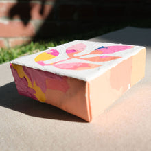 Load image into Gallery viewer, An angled close up of a colorful abstract painting with colors pink, yellow, orange, and some blue painted over with white to show a stem with leaves in the negative colored space. The painting is laying on a tan canvas outdoors.