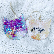 Load image into Gallery viewer, two cat shaped acrylic ornaments with gold ribbon. Left ornament has shades of blue, purple, and gold with "Willow 2021" painted on. Right ornament is shades of orange, yellow, and white with "Blaze 2021" painted on.