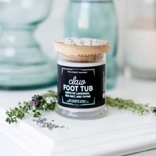 Load image into Gallery viewer, 7th Street Salvage's Claw Foot Tub candle sitting on a white counter with lavender sitting next to it. The candle label is black with white typography and the container has a wooden lid.