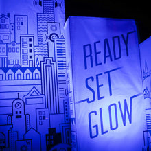 Load image into Gallery viewer, Photo of fabric banners, left has a graphic design of a cityscape and the right says "ready set glow" with a blue light tint