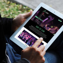 Load image into Gallery viewer, Photo of a man's hands holding an ipad on "5k dance party" website with blurred greenery and sidewalk in the background
