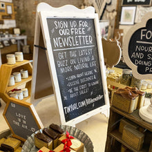 Load image into Gallery viewer, A small white chalkboard easel on top of a table. The lettering tells people how to sign up for The Bearded Bee's newsletter.