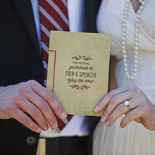 Load image into Gallery viewer, Man in suit and woman in white dress both holding a card together with text "the official guidebook to Erin & Spencer tying the knot"