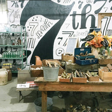 Load image into Gallery viewer, Photo of 7th street salvage's mural on a white wall with black sevens and "th" in a collage style