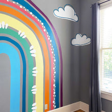 Load image into Gallery viewer, Final rainbow mural in A's bedroom. The rainbow is eggplant purple, navy blue salmon pink, orange, butter yellow, kelly green, navy, and cyan blue with white circle accents and flourishes. There are white clouds surrounding the rainbow with off centered navy outlines.