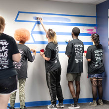 Load image into Gallery viewer, Five people painting horizontal lines at the start of the macon airport mural