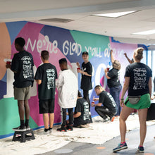 Load image into Gallery viewer, Group of people painting the macon airport mural white lettering with mama hawk draws in the foreground