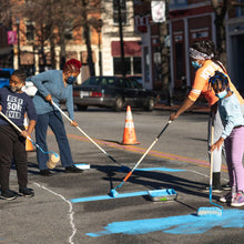 Load image into Gallery viewer, Two women and two children holding paint rollers and painting the sidewalk in blue paint