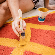 Load image into Gallery viewer, Woman's hand holding a paint brush with orange paint on it, painting orange lines on the crosswalk