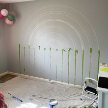 Load image into Gallery viewer, The beginning of E's rainbow mural. A dark gray wall with the rainbow stripes chalked out and painter's tape in place to begin painting.