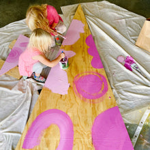 Load image into Gallery viewer, Mama Hawk Draws's two assistants paint light and dark pink shapes on the raw wood of the triangle tree for Macon's Museum of Arts and Science Festival of Trees.
