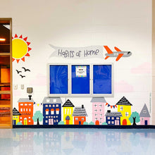 Load image into Gallery viewer, Front view of the "habits at home" mural with a sun and birds on the left and buildings and trees at the bottom of the wall