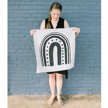 Load image into Gallery viewer, Erin from Mama Hawk Draws holds a 2'x2' cream colored drop cloth with a black rainbow painted on it. The rainbow has different widths of stripes. The interior stripe is the thickest, about 3", the next stripe is made of medium sized circles, the third stripe is about 2" thick, the 4th stripe is about 1" thick, and the last stripe is about 0.5" thick.