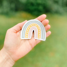 Load image into Gallery viewer, Hand holding a pink, yellow, and blue rainbow magnet with greenery in the background