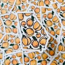 Load image into Gallery viewer, State of Georgia shaped sticker with peach design within the borders. The background is a collage of the same sticker.