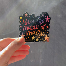 Load image into Gallery viewer, Woman holding a black sticker with colorful hologram hand lettering that reads "you are made of magic" with stars.