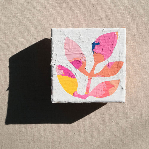 A colorful abstract painting with colors pink, yellow, orange, and some blue painted over with white to show a stem with leaves in the negative colored space. The painting is laying on a tan canvas.