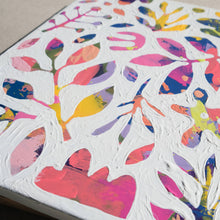 Load image into Gallery viewer, A closeup of a colorful abstract painting painted over with white to show designs of plants and nature in the negative space. The painting is laying on a tan canvas.
