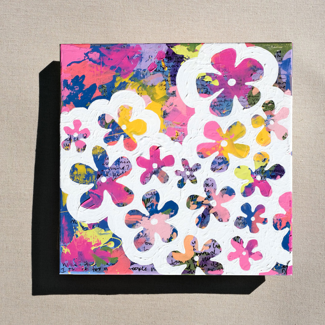 A colorful abstract painting painted over with white to show designs of flowers in the negative space. The painting is laying on a tan canvas.