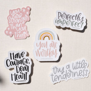 Five stickers with messages of empowerment, "you are stronger than you think", "perfectly imperfect", "have courage, dear heart", "try a little tenderness", and "you are worthy".