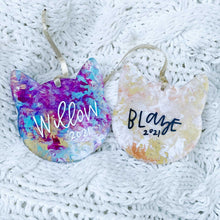 Load image into Gallery viewer, two cat shaped acrylic ornaments with gold ribbon. Left ornament has shades of blue, purple, and gold with &quot;Willow 2021&quot; painted on. Right ornament is shades of orange, yellow, and white with &quot;Blaze 2021&quot; painted on.
