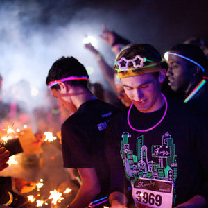 photo of group of men in glow stick decorations with smoke and sparklers in the background