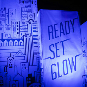 Photo of fabric banners, left has a graphic design of a cityscape and the right says "ready set glow" with a blue light tint