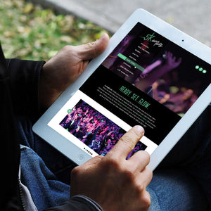 Photo of a man's hands holding an ipad on "5k dance party" website with blurred greenery and sidewalk in the background