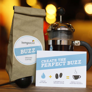 Living social paper bag with sticker logo with "BUZZ ground coffee" text. French press on the right of the bag and coffee scoop under the bag. Card with "create the perfect buzz" to the right of the scoop