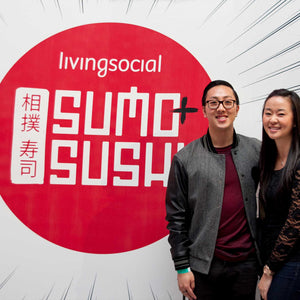 Photo of an asian man and a women standing together against the living social sumo sushi advertisement enlarged in the background 