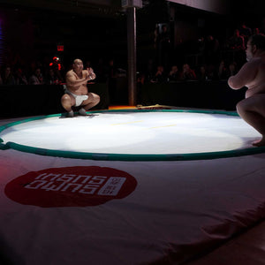 Photo of a sumo wrestling ring with two sumo wrestlers assuming form for their match in dim lighting