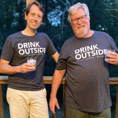 Two white men holding drinks with grey tees with 