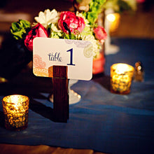 Load image into Gallery viewer, Photo of a table setting with blue cloth, two candles and a bouquet of flowers in the background. A clothespin holding a card with text &quot;table 1&quot; with colorful paisley edges in the center
