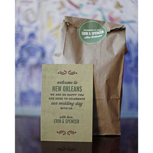 card with text "welcome to new orleans" standing against brown paper bag enclosed by a green sticker with text "Erin & Spencer" on it