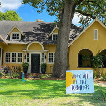 Load image into Gallery viewer, Street view of a yellow house with &quot;we&#39;re all in this together&quot; yard sign sitting in the grass in the bottom right. 
