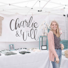 Load image into Gallery viewer, Owner, Kirsten McClendon, standing in front of her Charlie &amp; Will booth were she is selling her handmade goods for littles. Behind Kirsten is a large white banner with the handlettered logo in black.
