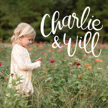 Load image into Gallery viewer, Handlettered white Charlie &amp; Will logo on a photo of a young girl standing in a zinna field of flowers wearing a Charlie and Will dress. 
