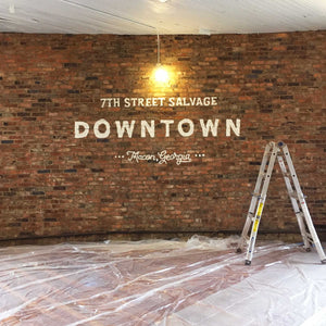 In the middle of installing the 7th Street Salvage Downtown mural. Only the white typography is installed, saying, "7th Street Salvage Downtown Macon, Georgia"