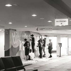 Black and white photo of seven people painting different parts of the macon airport mural
