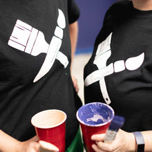 Load image into Gallery viewer, Shot of two people with black shirts on with white paintbrushes painted in the center, holding cups of paint and brushes
