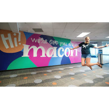 Load image into Gallery viewer, Mama Hawk Draws jumping in front of a full view of the macon airport mural
