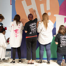 Load image into Gallery viewer, Close up of three women painting the white lettering in the word &quot;hi!&quot;of the macon airport mural
