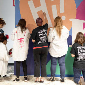 Close up of three women painting the white lettering in the word "hi!"of the macon airport mural